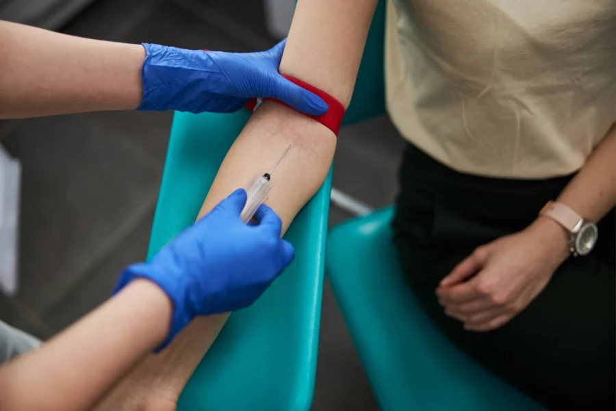 A gloved phlebotomist draws blood from a patient’s arm during lab work that helps assess the apolipoprotein B normal range.